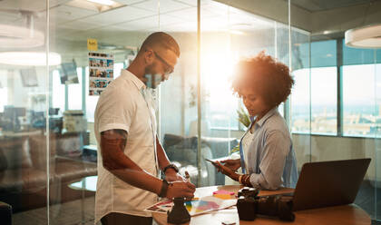 Zwei junge Fotografen besprechen den Aufnahmeplan am kreativen Arbeitsplatz. Design-Profis arbeiten in einem modernen Büro zusammen. - JLPSF00608