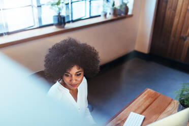 Draufsicht auf eine junge Frau, die an ihrem Schreibtisch sitzt und am Computer arbeitet. Afrikanische weibliche Führungskraft arbeitet im Büro. - JLPSF00611