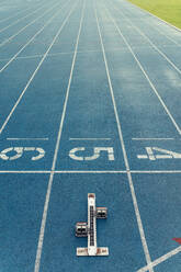 Starting block placed at the start line of a running track. Metal starting block isolated on a blue all-weather running track. - JLPSF00655