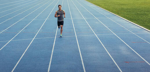 Sportler, der allein auf einer Allwetterlaufbahn läuft. Läufer, der auf einer blauen gummierten Laufbahn sprintet. - JLPSF00658