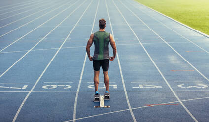 Rückansicht eines Athleten, der zum Sprint auf einer Allwetter-Laufbahn bereit ist. Ein Läufer benutzt einen Startblock, um seinen Lauf auf der Laufbahn zu beginnen. - JLPSF00660