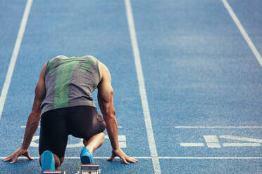 Rückansicht eines Athleten, der zum Sprint auf einer Allwetter-Laufbahn bereit ist. Ein Läufer benutzt einen Startblock, um seinen Lauf auf der Laufbahn zu beginnen. - JLPSF00662