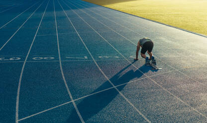 Rückansicht eines Athleten, der zum Sprint auf einer Allwetter-Laufbahn bereit ist. Ein Läufer benutzt einen Startblock, um seinen Lauf auf der Laufbahn zu beginnen. - JLPSF00663