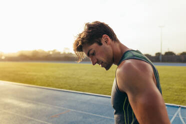 Closeup of a sprinter standing on a running track. Athlete looking down at the track. - JLPSF00665