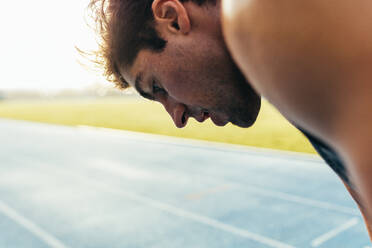Nahaufnahme eines Sprinters, der auf einer Laufbahn steht. Ein müder Sportler entspannt sich nach einem Lauf auf der Laufbahn. - JLPSF00670