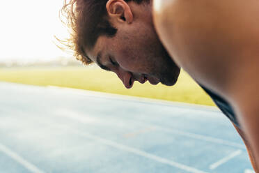 Nahaufnahme eines Sprinters, der auf einer Laufbahn steht. Ein müder Sportler entspannt sich nach einem Lauf auf der Laufbahn mit geschlossenen Augen. - JLPSF00671