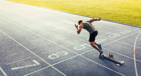 Rückansicht eines Athleten, der seinen Sprint auf einer Allwetter-Laufbahn beginnt. Ein Läufer benutzt einen Startblock, um seinen Lauf auf der Laufbahn zu beginnen. - JLPSF00672