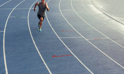 Sportler, der allein auf einer Allwetterlaufbahn läuft. Läufer, der auf einer blauen gummierten Laufbahn sprintet. - JLPSF00673