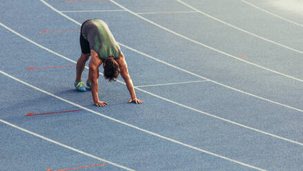 Athlete doing stretching exercises on the running track. Runner stretching muscles by touching the hands on the track. - JLPSF00674