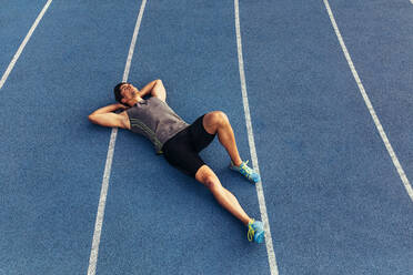 Ein Läufer liegt entspannt auf der Bahn und hat die Hände unter dem Kopf. Ein Sportler entspannt sich nach einem Lauf. - JLPSF00676