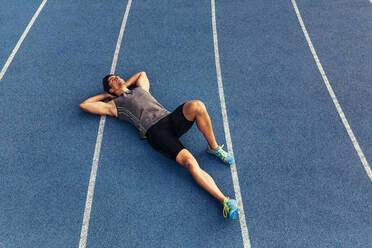 Runner lying on the track in a relaxed mood with hands under his head. Athlete relaxing after a run. - JLPSF00676