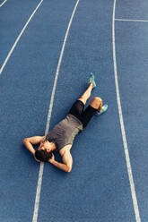 Ein Läufer liegt entspannt auf der Bahn und hat die Hände unter dem Kopf. Draufsicht eines Sportlers, der sich nach einem Lauf entspannt. - JLPSF00677