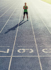 Runner standing on running track with hands folded. Athlete wearing earphones with mobile phone fixed in arm band. - JLPSF00678