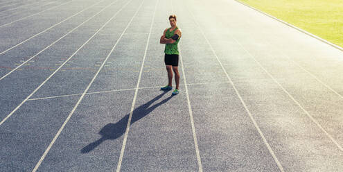 Runner standing on running track with hands folded. Athlete wearing earphones with mobile phone fixed in arm band. - JLPSF00680