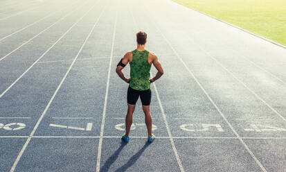 Rear view of an athlete standing on an all-weather running track. Runner standing at the start line with hands on waist. - JLPSF00682