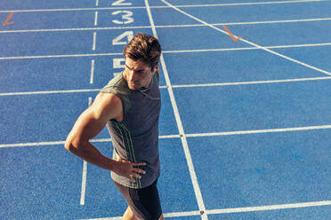 Athlete standing on a running track near the start line. Runner wearing earphones walking on the running track. - JLPSF00688