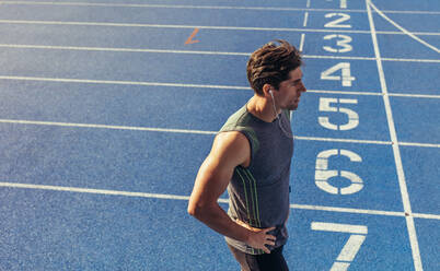 Athlete standing on a running track near the start line. Runner wearing earphones standing on the running track. - JLPSF00689