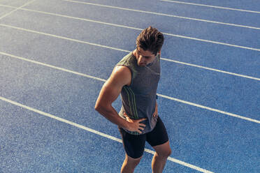 Athlete walking on a running track listening to music. Runner wearing earphones walking on the running track. - JLPSF00691