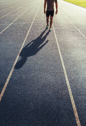 Sportler, der auf einer Allwetter-Laufbahn läuft und dabei Musik hört. Schatten eines Läufers, der auf der Bahn läuft. - JLPSF00694