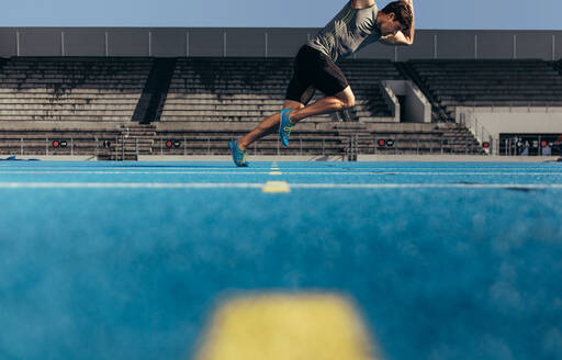 Side view of an athlete starting his sprint on an all-weather running track. Runner practicing his sprint on a running track in a stadium. - JLPSF00710