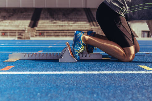 Athlete on his mark ready to sprint on an all-weather running track. Runner using a starting block to start his run on race track. - JLPSF00711