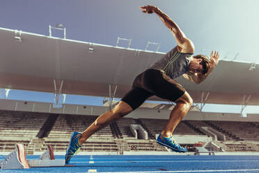Athlete starting his sprint on an all-weather running track. Runner using starting block to start his run on running track in a stadium. - JLPSF00712