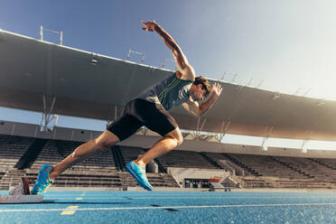 Läufer, der seinen Lauf auf einer Laufbahn in einem Stadion mit einem Startblock beginnt. Athlet, der seinen Sprint auf einer Allwetterlaufbahn beginnt. - JLPSF00713