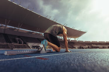 Rückansicht eines Athleten, der zum Sprint auf einer Laufbahn bereit ist. Ein Läufer benutzt einen Startblock, um seinen Lauf auf einer Laufbahn in einem Stadion zu beginnen. - JLPSF00714