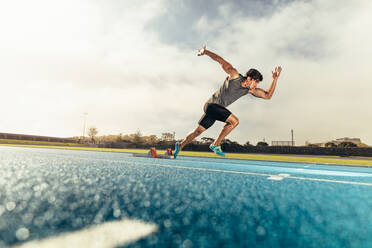 Läufer, der seinen Lauf auf einer Laufbahn mit Hilfe eines Startblocks beginnt. Sportler, der seinen Sprint auf einer Allwetterlaufbahn mit Hilfe eines Startblocks beginnt. - JLPSF00715