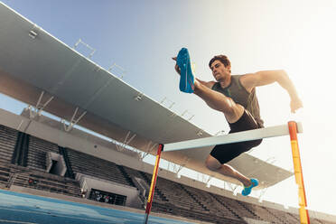 Nahaufnahme eines Läufers, der bei einem Leichtathletikwettkampf über eine Hürde springt. Ein Athlet läuft einen Hürdenlauf in einem Stadion. - JLPSF00718