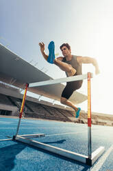 Läufer, der bei einem Leichtathletikwettkampf über eine Hürde springt. Athlet, der einen Hürdenlauf in einem Stadion absolviert. - JLPSF00719