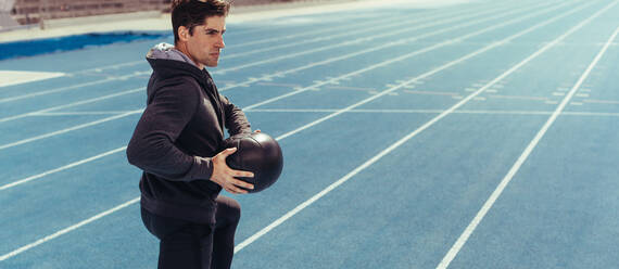 Runner doing a medicine ball workout on running track. Athlete using a medicine ball for fitness training at a track and field stadium. - JLPSF00721