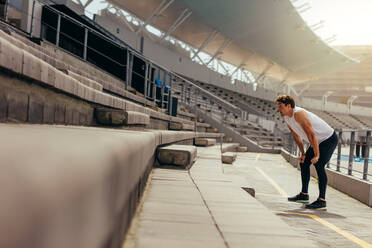Sportler beim Training auf der Tribüne eines Leichtathletikstadions. Läufer steht mit den Händen auf den Knien auf der Tribüne. - JLPSF00727
