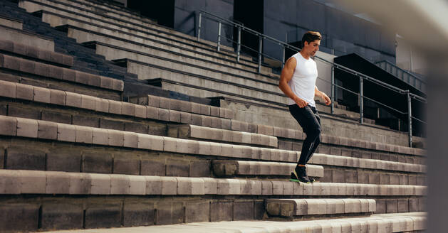 Läufer, der im Rahmen seines körperlichen Trainings die Stufen der Stadiontribüne hinunterläuft. Junger Mann, der die Stufen des Stadions hinunterläuft. - JLPSF00728