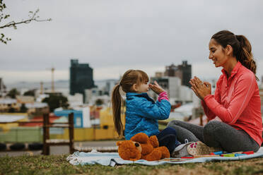 Side view of happy smiling woman and a girl child playing patty-cake game while sitting at a park. Little girl playing clapping game with her nanny outdoors. - JLPSF00736