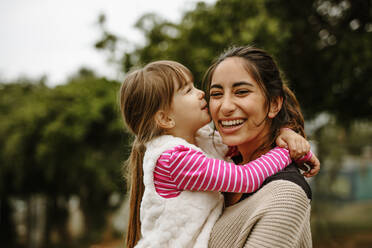 Girl kissing on the cheek of her nanny at the park. Babysitter having fun with a girl at the park. - JLPSF00742