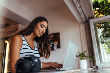 Frau Blogger mit Laptop zu Hause mit Kopfhörern. Frau sitzt mit einer professionellen Kamera auf dem Tisch arbeiten auf ihrem Laptop-Computer. - JLPSF00778