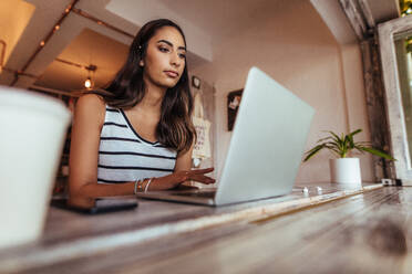 Frau Bloggerin arbeitet an Laptop zu Hause. Frau sitzt mit Kaffeeglas und Handy auf dem Tisch und arbeitet an ihrem Laptop-Computer. - JLPSF00782