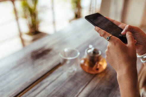 Nahaufnahme einer Frau, die eine gläserne Teekanne und ein leeres Glas mit einem Mobiltelefon für ihren Food-Blog fotografiert. Food-Bloggerin beim Fotografieren für ihren Blog. - JLPSF00784