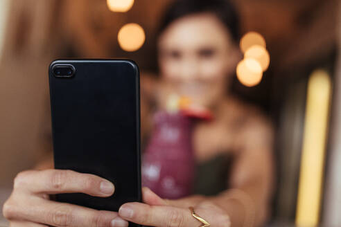 Unscharfes Bild einer Frau, die mit einem Mobiltelefon ein Selfie mit einem Smoothie auf dem Tisch macht. Food-Bloggerin, die zu Hause Fotos für ihren Blog schießt. - JLPSF00799