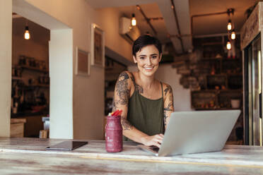 Frau Unternehmerin arbeitet auf Laptop-Computer zu Hause mit einem Smoothie auf dem Tisch. Frau genießt ein Glas Smoothie während der Arbeit zu Hause. - JLPSF00803