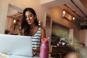 Frau Unternehmerin arbeitet am Laptop mit einem Smoothie auf dem Tisch. Frau genießt ein Glas Smoothie während der Arbeit. - JLPSF00805