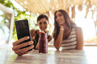 Zwei Frauen sitzen in einem Restaurant mit einem Smoothie auf dem Tisch und fotografieren. Frau schießt Selfie mit einem Freund in einem Restaurant. - JLPSF00815