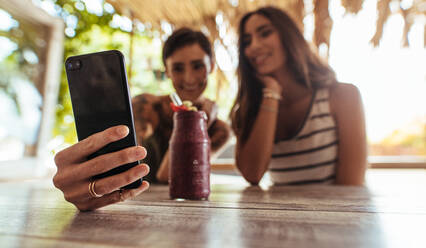 Zwei Frauen sitzen in einem Restaurant mit einem Smoothie auf dem Tisch und fotografieren. Frau schießt Selfie mit einem Freund in einem Restaurant. - JLPSF00816