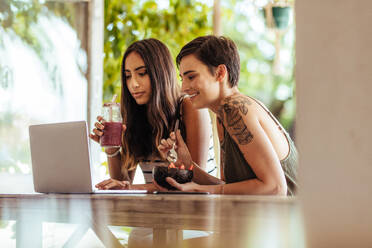 Two women sitting at a restaurant working on a laptop computer. Women sitting at a restaurant enjoying smoothie and a dessert. - JLPSF00825
