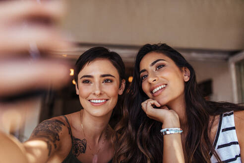 Zwei Frauen sitzen im Freien und schauen auf ein Mobiltelefon. Lächelnde Frauen posieren für ein Selfie. - JLPSF00829