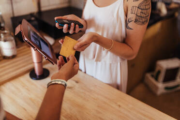 Ein Kunde bezahlt die Rechnung in einem Café mit einer Kreditkarte. Eine Unternehmerin hält ein drahtloses Kassengerät, um eine Kartentransaktion durchzuführen. - JLPSF00835