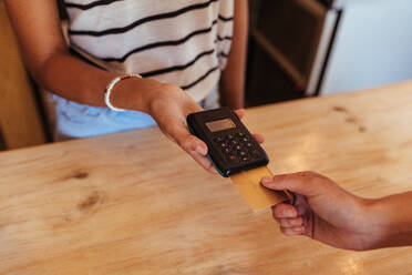 Woman entrepreneur using a wireless point of sale machine to effect a cashless payment. Close up of a woman holding a wireless point of sale machine while a card is inserted. - JLPSF00837