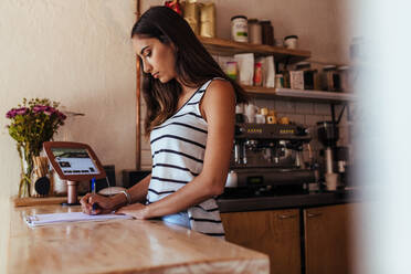 Eine Frau steht an der Abrechnungstheke ihres Cafés und notiert die Bestellungen. Ein Restaurantbesitzer macht sich Notizen an der Abrechnungstheke. - JLPSF00839