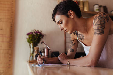 Eine Frau, die an der Theke ihres Cafés steht und Bestellungen notiert. Ein Restaurantbesitzer macht sich Notizen an der Abrechnungstheke. - JLPSF00844